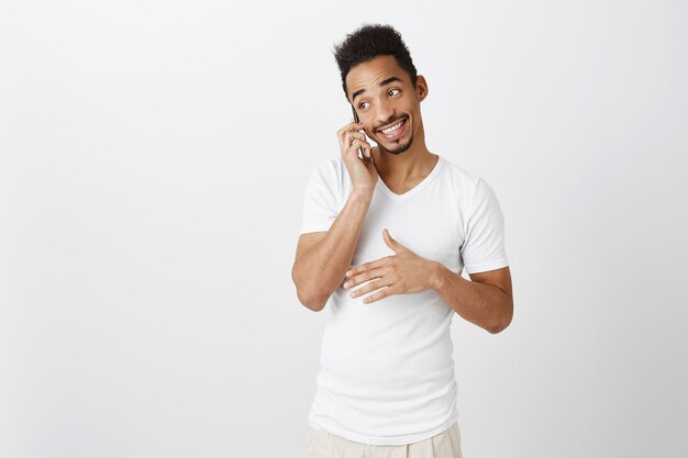 Wychodzący przystojny Murzyn w białej koszulce rozmawia przez telefon, uśmiechnięta, szczęśliwa rozmowa