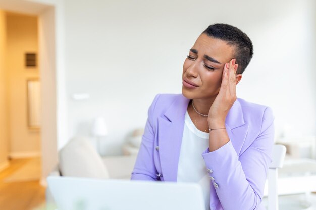 Wyczerpana kobieta z bólem głowy w domowym biurze Kreatywna Afroamerykanka pracująca przy biurku czuje się zmęczona Zestresowana kobieta biznesu odczuwa ból oczu podczas przepracowania