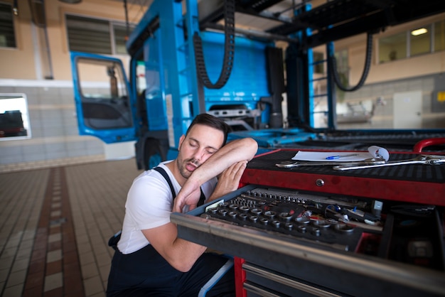Bezpłatne zdjęcie wyczerpany mechanik samochodowy zasypia w swoim warsztacie