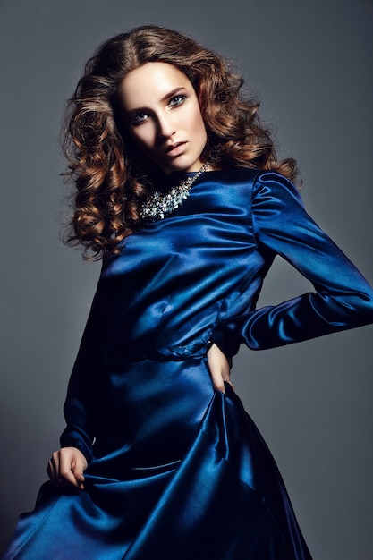 Wygląd mody. glamour portret pięknej stylowej brunetki młodej kobiety rasy kaukaskiej z jasnym makijażem, ze zdrowymi kręconymi włosami w jasnej niebieskiej sukience