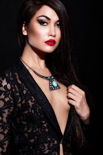 Wygląd mody. Seksowny portret pięknej seksownej stylowej brunetki młodej kobiety rasy kaukaskiej z jasnym makijażem, z czerwonymi ustami, z idealnie czystą skórą z biżuterią w czarnej tkaninie
