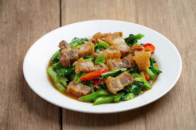 Wymieszaj smażony jarmuż, pikantną chrupiącą wieprzowinę na drewnianym stole. Koncepcja tajskiego jedzenia.
