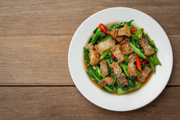 Wymieszaj smażony jarmuż, pikantną chrupiącą wieprzowinę na drewnianym stole. Koncepcja tajskiego jedzenia.