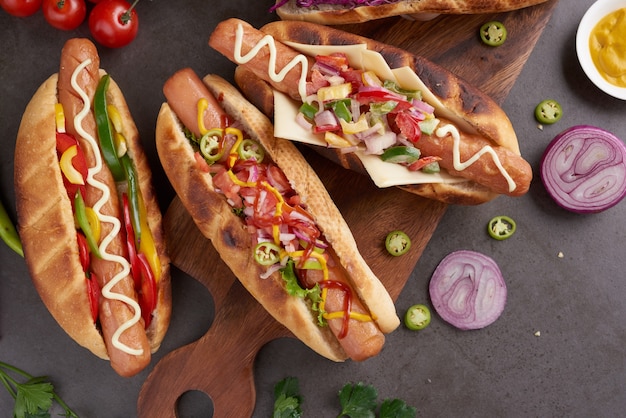 Wyśmienity grillowany cały hot dog wołowy z dodatkami i frytkami. Pyszne i proste hot dogi z musztardą, papryką, cebulą i nachos. Hot dogi w pełni załadowane różnymi dodatkami na desce do wiosła.