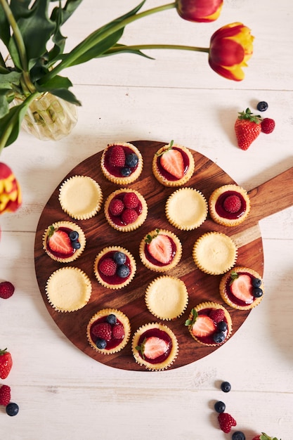 Bezpłatne zdjęcie wysoki kąt strzału cupcakes sera z galaretką owocową i owocami na drewnianym talerzu