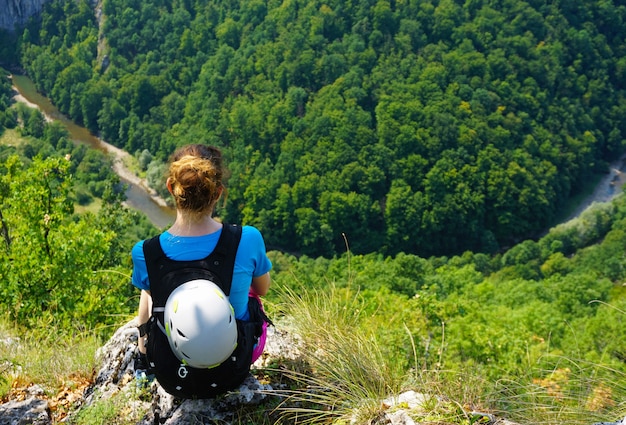 Wysoki kąt strzału kobiet turysta siedzący na skraju klifu, patrząc w dół na las