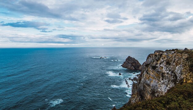 Wysoki kąt strzału morza w pobliżu góry pod zachmurzonym niebem w Cabo Penas, Asturia, Hiszpania