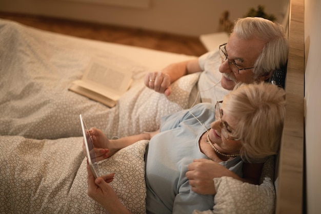 Wysoki kąt widzenia starszej pary korzystającej z cyfrowego tabletu podczas leżenia w łóżku w nocy