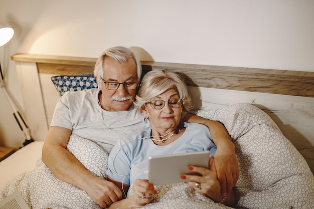 Wysoki kąt widzenia starszej pary korzystającej z touchpada podczas odpoczynku w sypialni