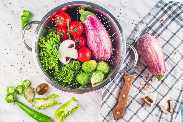 Wysokiego kąta widok zdrowi organicznie warzywa w colander nad marmurowym tłem