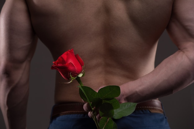 Wysportowany mężczyzna trzyma czerwoną różę za plecami. koncepcja relacji miłości i romansu