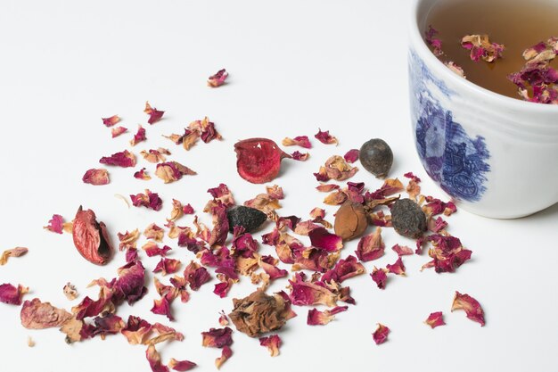 Wysuszeni różani płatki i herbaciana filiżanka odizolowywająca na białym tle