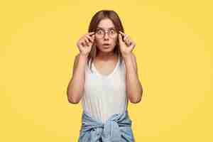 Bezpłatne zdjęcie wzruszający, przerażony młoda brunetka w okularach pozuje na żółtej ścianie