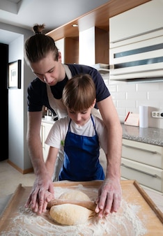 Yong mężczyzna i dziecko wyrabiają ciasto do pieczenia bułeczek na tle domowej kuchni
