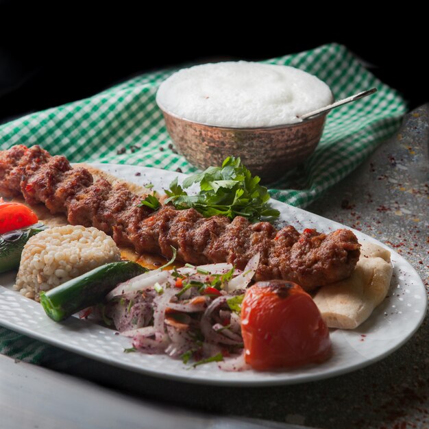 Z góry kebab adana z ryżem i smażonymi warzywami oraz posiekaną cebulą i ayranem