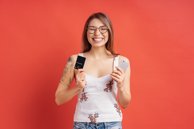 Z podnieceniem ładna młoda kobieta trzyma telefon i kartę kredytową w jej rękach
