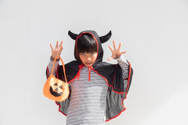 Zabawna koncepcja halloweenowego dziecka, mała urocza dziewczyna z kostiumem halloweenowym duchem przerażającym, który trzyma pod ręką pomarańczowego ducha dyni, na białym tle