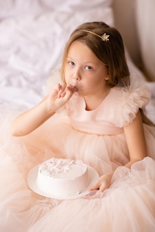Zabawna księżniczka dziecko dziewczynka świętująca urodziny je kremowe ciasto w łóżku