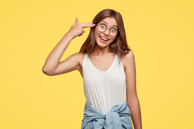 Zabawna młoda brunetka w okularach, pozowanie na żółtej ścianie