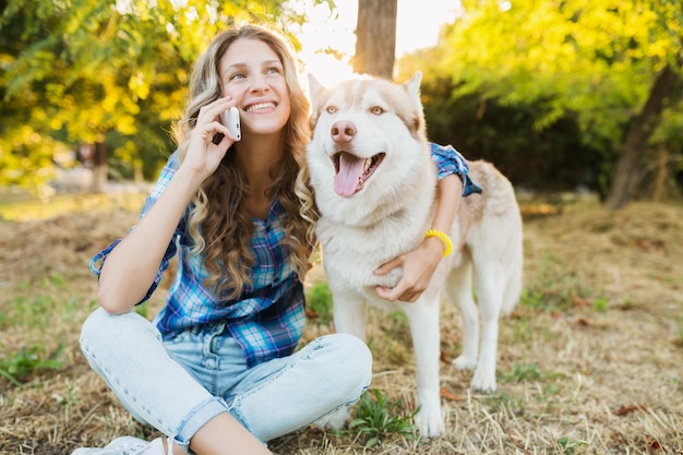 Zabawna młoda ładna kobieta bawi się z psem rasy husky w parku w słoneczny letni dzień