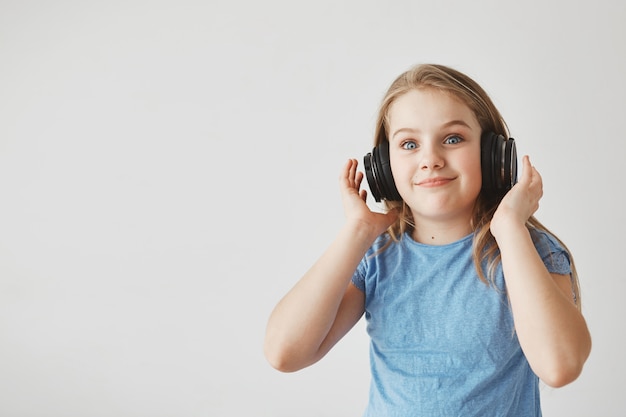 Bezpłatne zdjęcie zabawna wesoła dziewczyna o jasnych włosach i niebieskich oczach, nosząca słuchawki. ze zszokowanym wyrazem twarzy, gdy nagle zaczyna grać głośna muzyka