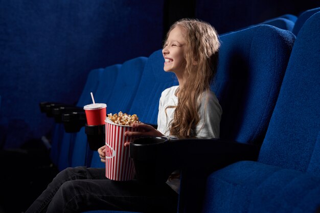 Zabawne dziecko trzymające popcorn i śmiejące się z komicznego filmu