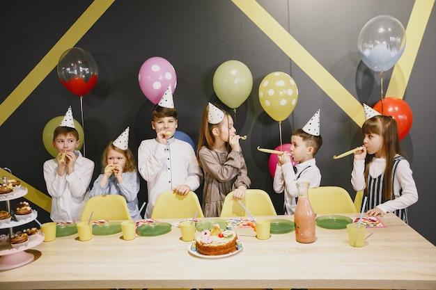 Zabawne przyjęcie urodzinowe dla dzieci w urządzonym pokoju. Szczęśliwe dzieciaki z ciastem i balonami.