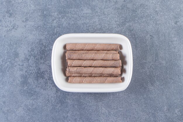 Ząbkująca czekoladowa rolka waflowa w misce, na marmurowym tle.
