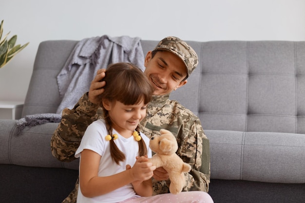 Zachwycony, przystojny młody dorosły żołnierz w mundurze kamuflażowym, wracający do domu po wojsku, spędzający czas z córką, witający rodzinę ojca, cieszący się, że widzi tatę.