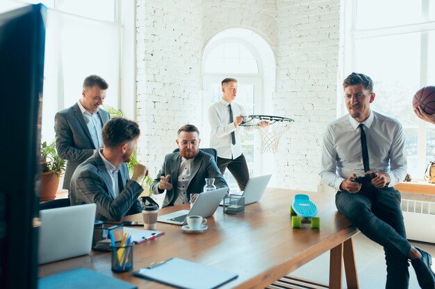 Zadowoleni, beztroscy koledzy bawią się w biurze, podczas gdy ich współpracownicy ciężko pracują i bardzo skoncentrowani.