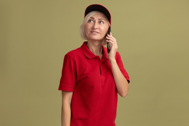 Zadowolona blondynka w średnim wieku w czerwonym mundurze i czapce rozmawia przez telefon patrząc w górę
