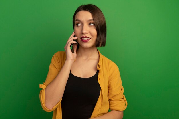 Zadowolona ładna kaukaska kobieta rozmawia przez telefon, patrząc z boku na zielono