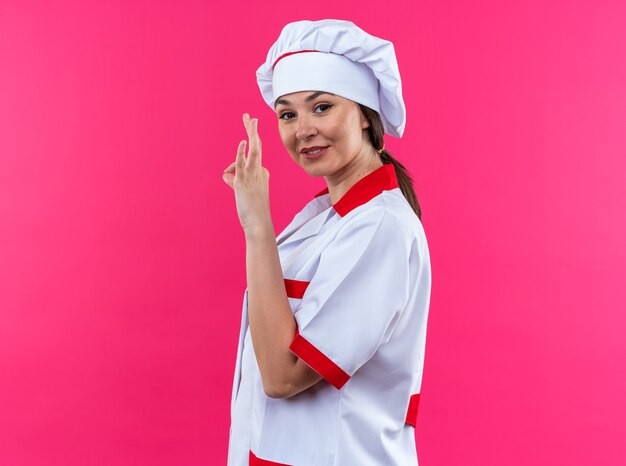 Zadowolona młoda kobieta kucharz ubrana w mundur szefa kuchni pokazująca dębowy gest na różowym tle