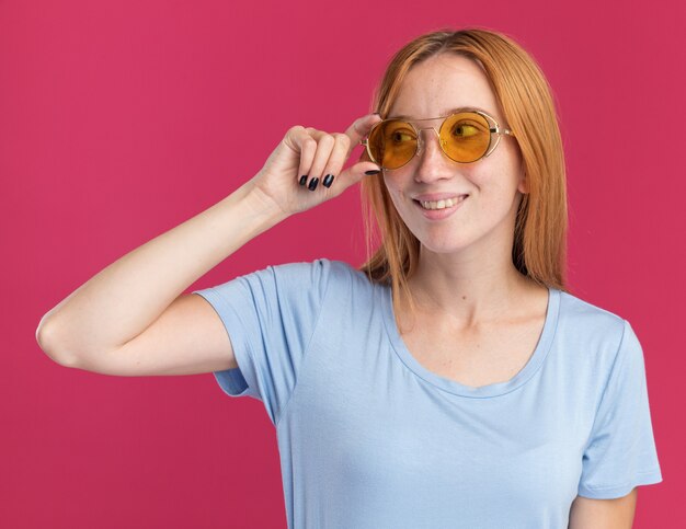 Zadowolona młoda rudowłosa dziewczyna z piegami w okularach przeciwsłonecznych, patrząc z boku
