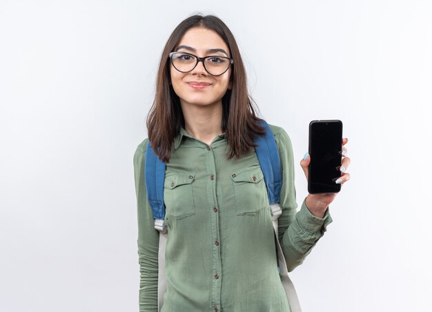 Zadowolona młoda szkolna kobieta w okularach z plecakiem trzymająca telefon