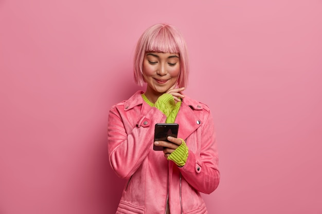 Bezpłatne zdjęcie zadowolona urocza blogerka społecznościowa ze stylową fryzurą, trzyma smartfona, czyta artykuł w internecie