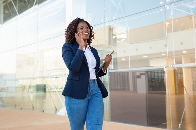 Zadowolony bizneswoman chodzi i opowiada smartphone