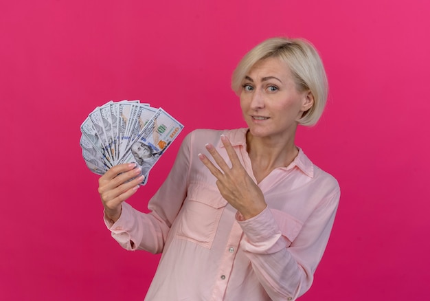 Zadowolony młoda blond słowiańska kobieta trzyma pieniądze na białym tle na różowym tle