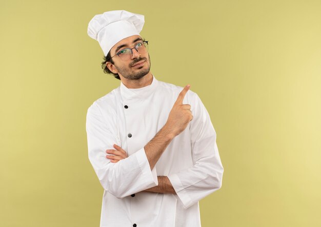 zadowolony młody kucharz w mundurze szefa kuchni i okularach wskazuje na bok