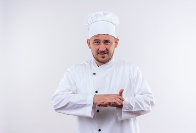 Zadowolony młody przystojny kucharz w mundurze szefa kuchni, trzymając ręce razem na białym tle na białej przestrzeni