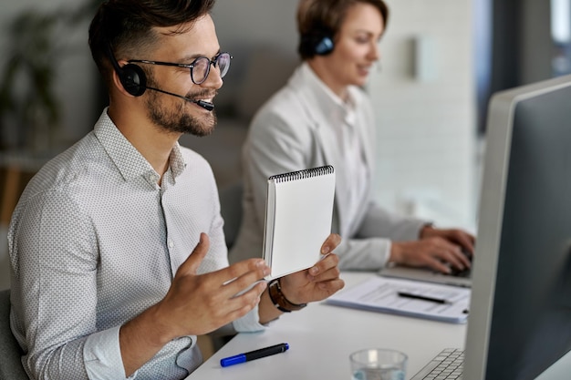 Zadowolony przedstawiciel obsługi klienta korzystający z komputera i prowadzący wideorozmowę z klientami podczas pracy w call center