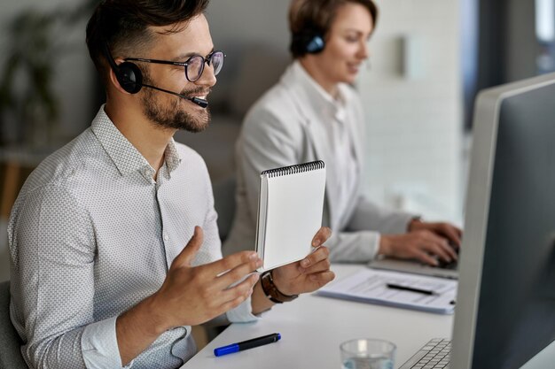 Zadowolony przedstawiciel obsługi klienta korzystający z komputera i prowadzący wideorozmowę z klientami podczas pracy w call center