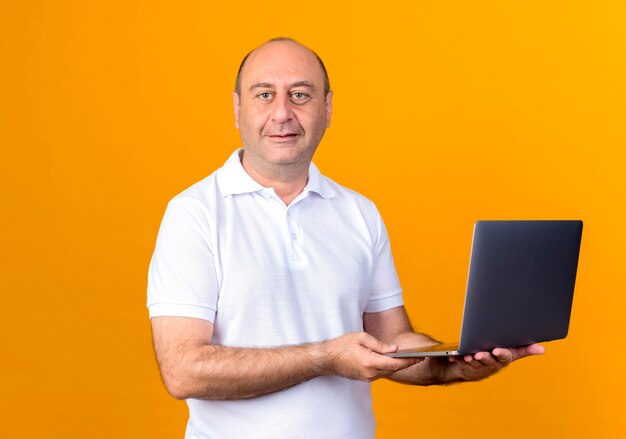 Zadowolony przypadkowy dojrzały mężczyzna trzyma laptopa na białym tle na żółtym tle