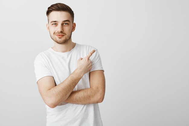 Zadowolony przystojny młody mężczyzna w białej koszulce, wskazując palcem w prawym górnym rogu