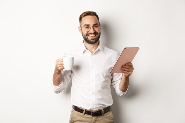 Zadowolony szef pijący herbatę i korzystający z tabletu cyfrowego, czytający lub pracujący, na stojąco