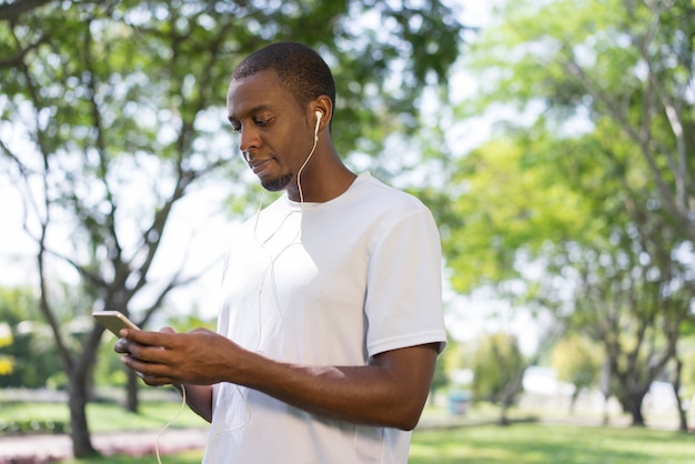 Zadumany dysponowany czarnego faceta położenia playlista na smartphone w parku.