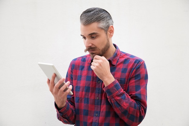 Zadumany mężczyzna z ręką na brodzie przy użyciu komputera typu tablet