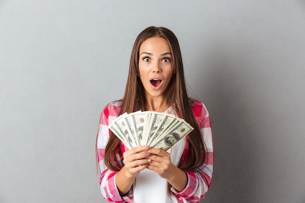 Bezpłatne zdjęcie zadziwiająca piękna młoda brunetki kobieta w kraciastej koszula trzyma pieniądze