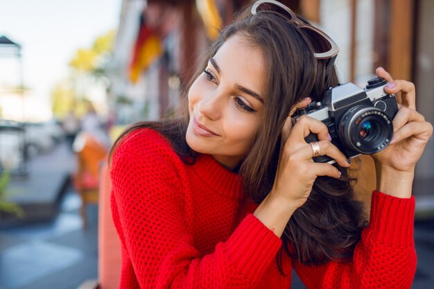 Zainspirowana brunetka, która dobrze się bawi i robi zdjęcia podczas wakacji. Zimny sezon. Ubrana w stylowy czerwony sweter z dzianiny.