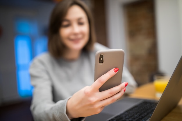 Zajęty Kobieta pracująca w domu na komputerze przenośnym i zadzwonić na jej telefon